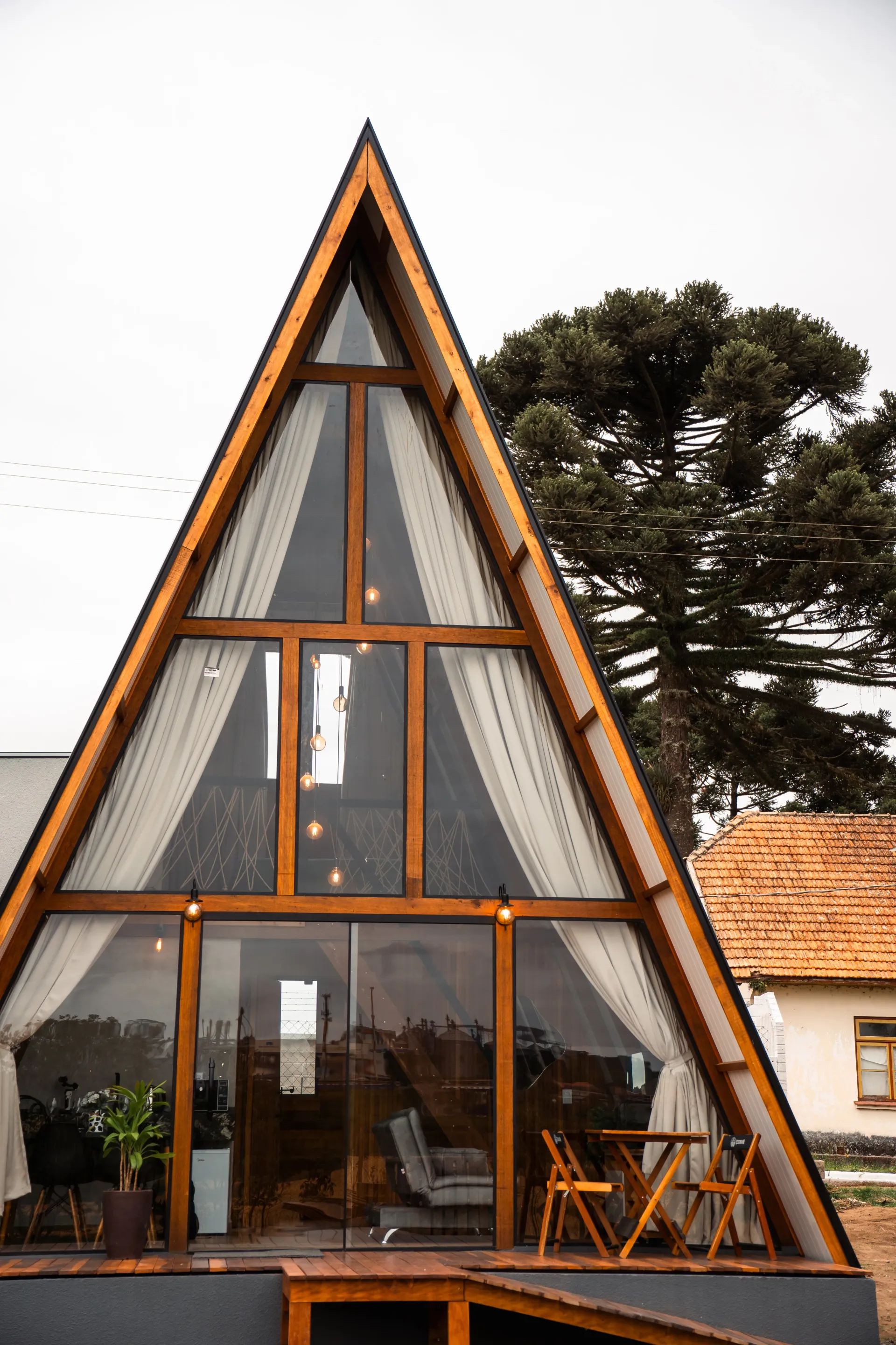 Cabine triangular com janelas grandes e estrutura de madeira; mesa e cadeiras no convés. Chalé Mont Hermon.