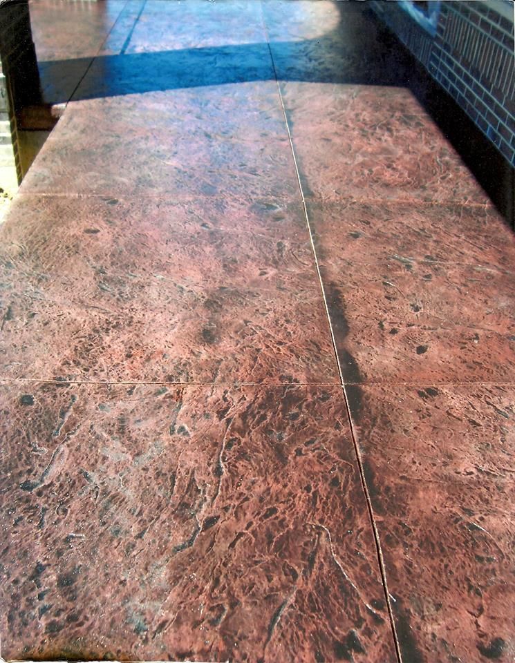 Stamped concrete walkway with red and brown mottled pattern; sunlight casts shadows.