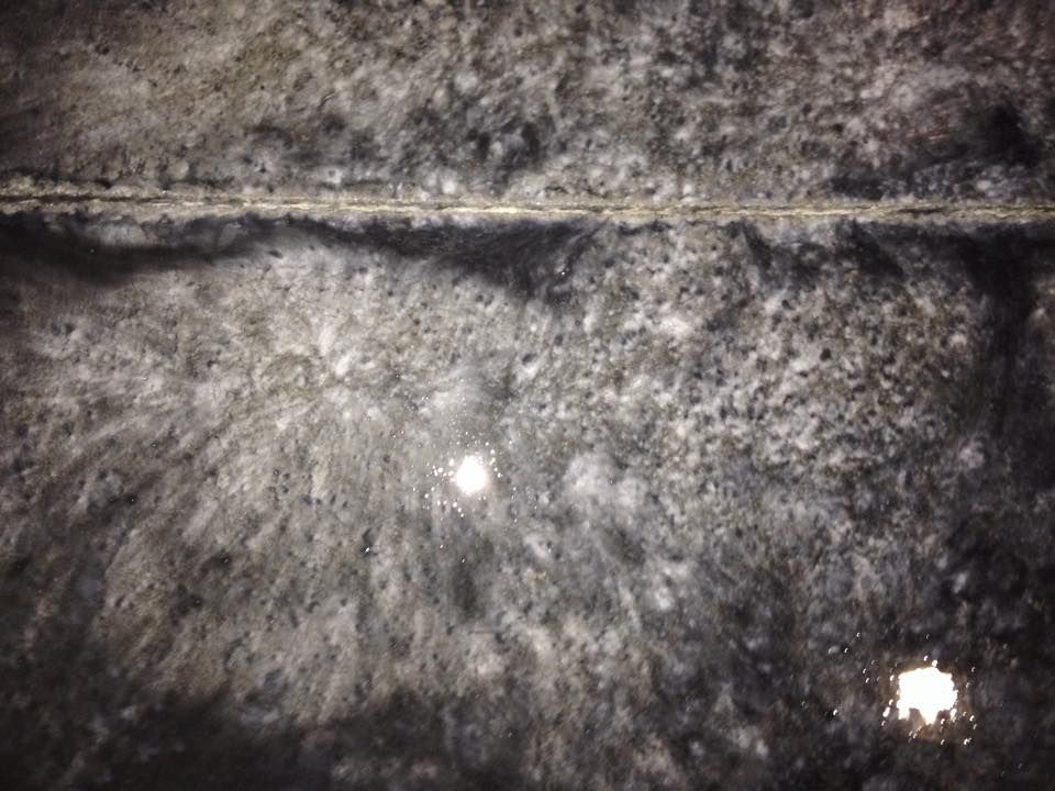 Close-up of dark, speckled surface with a light-colored line through the middle and small reflective spots.