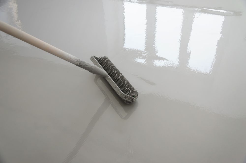 A person using a brush to smooth out wet, light-colored flooring.