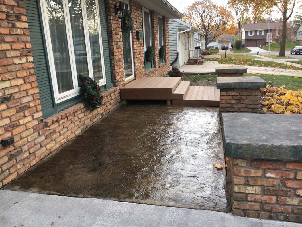 Brick house entrance with wet concrete landing, wooden deck, and brick pillars.