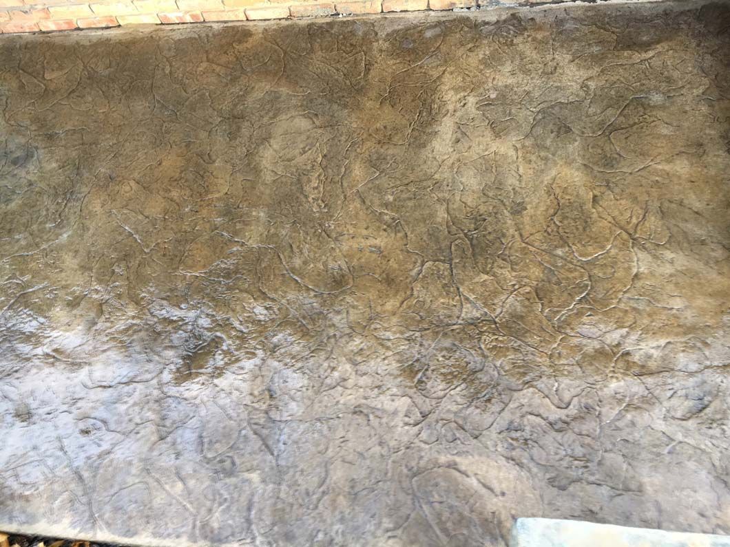 Textured concrete floor, transitioning from dark brown to gray, possibly outdoors.