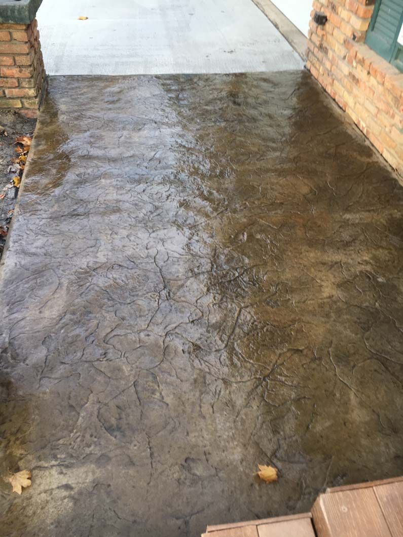 Dark brown textured concrete walkway, wet with water; brick walls on either side.