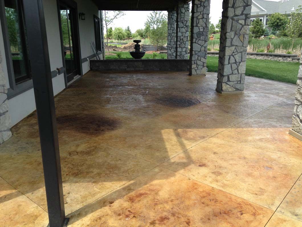 Covered patio with stained concrete floor, dark stains, and stone columns.