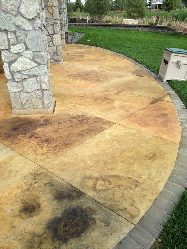 Stone patio with stained concrete, circular shape, next to a grassy lawn and a stone column.