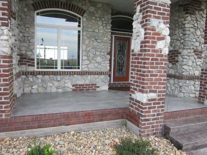 Exterior of a house with stone and brick facade, arched window, and small porch.