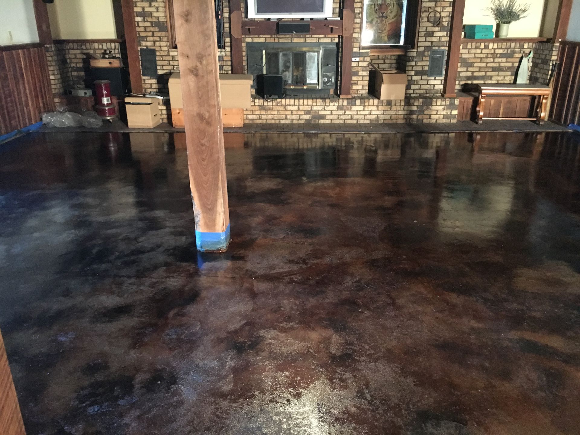 Polished brown and tan stained concrete floor in a room with a brick fireplace and wooden support beam.