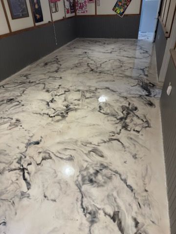 Marble-effect epoxy floor in a room. Black and white swirling patterns reflect light. Gray and wooden walls.