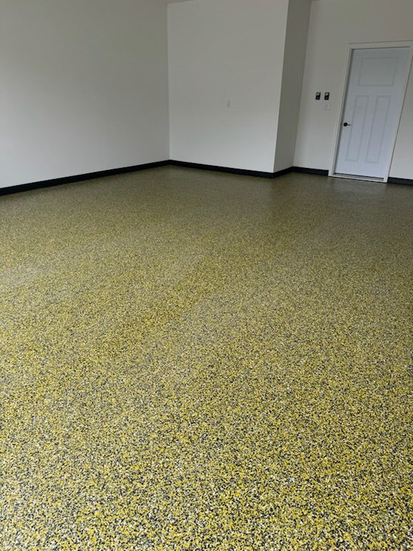 Empty garage with yellow, black, and white speckled epoxy floor. White walls and door.