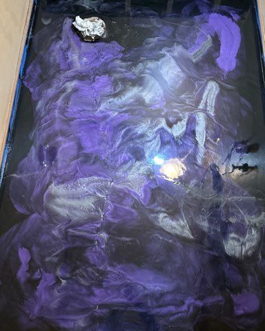 Abstract resin art in shades of purple, silver, and black, with a rock embedded.