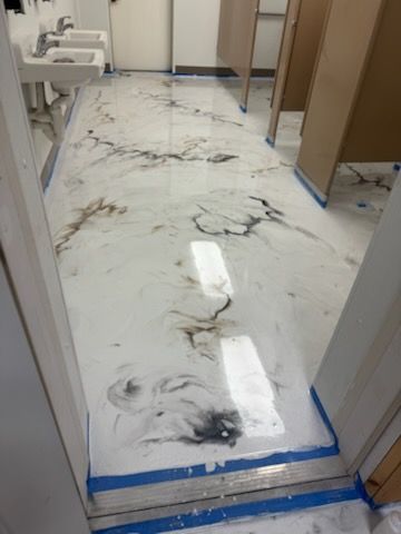 Epoxy floor in a public restroom. White and black marbled effect, sinks and stalls visible.