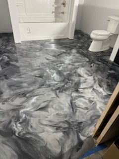 Bathroom with gray and white swirled epoxy floor; tub, toilet, and partially visible wall.