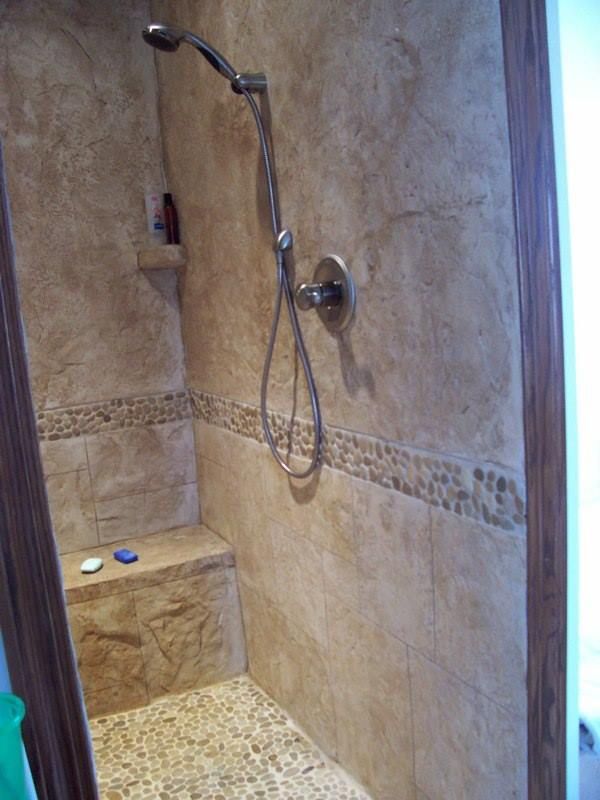 Shower with stone tile walls, pebble floor, built-in bench, and shower head. Brown, beige tones.