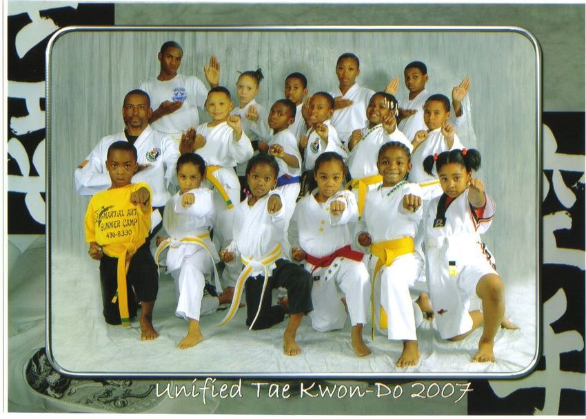 Group of children in white and yellow martial arts uniforms posing on a stage