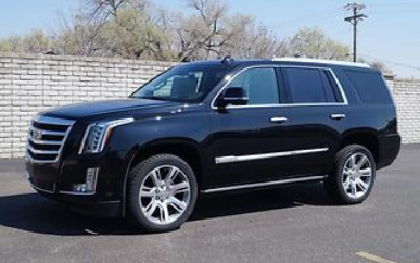 A black Cadillac Escalade SUV parked on asphalt in front of a white brick wall.