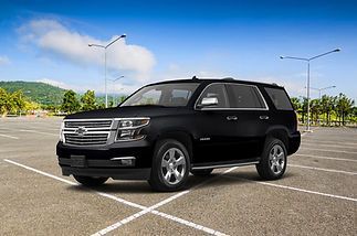 A black Chevrolet Tahoe SUV parked in a large, empty asphalt parking lot under a blue sky with light clouds.