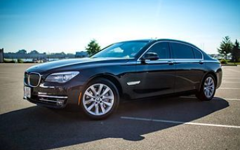 A dark-colored BMW sedan parked in an empty outdoor parking lot on a sunny day.