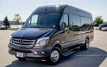 A shiny black Mercedes-Benz Sprinter luxury passenger van parked in a sunny, paved parking lot.