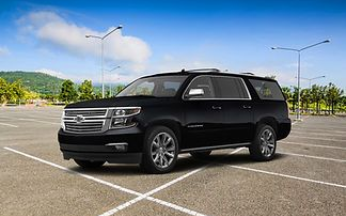 A black Chevrolet Suburban parked in a large, empty outdoor parking lot under a blue sky.