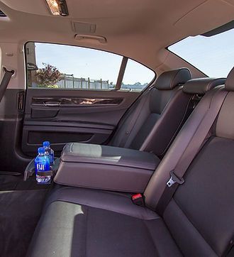 The dark interior of a car back seat with leather upholstery and two bottles of Fiji water in the side door pocket.