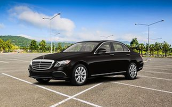 A black Mercedes-Benz sedan parked in an empty asphalt lot under a blue sky with hills in the background.