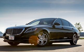 A black Mercedes-Benz sedan parked on asphalt under a clear, bright sky.
