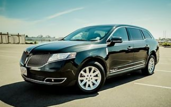 A black Lincoln MKT crossover vehicle parked in an empty outdoor parking lot under a bright, clear blue sky.