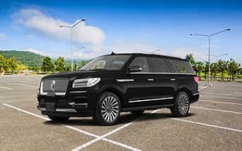 A black Lincoln Navigator SUV parked in an empty outdoor parking lot under a blue sky.