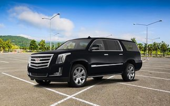 A black Cadillac Escalade SUV parked in an empty outdoor lot on a sunny day.