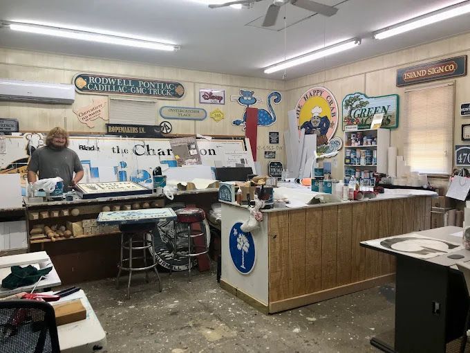 Cluttered shop interior with a man behind the counter, wall signs, and shelves of merchandise
