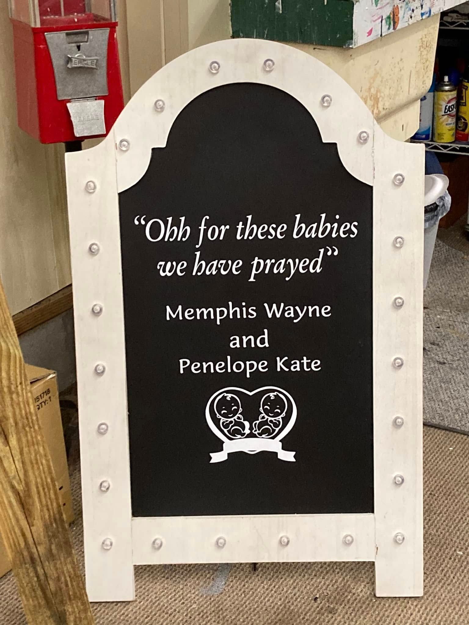 Memorial plaque on a black sign with white border reading, “Oh for the babies we have prayed” and two names.
