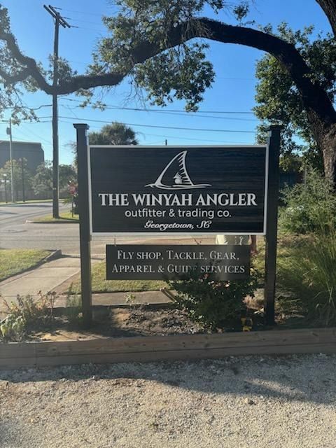 Sign for The Winyah Angler outfitter and trading co. under a tree by the roadside.