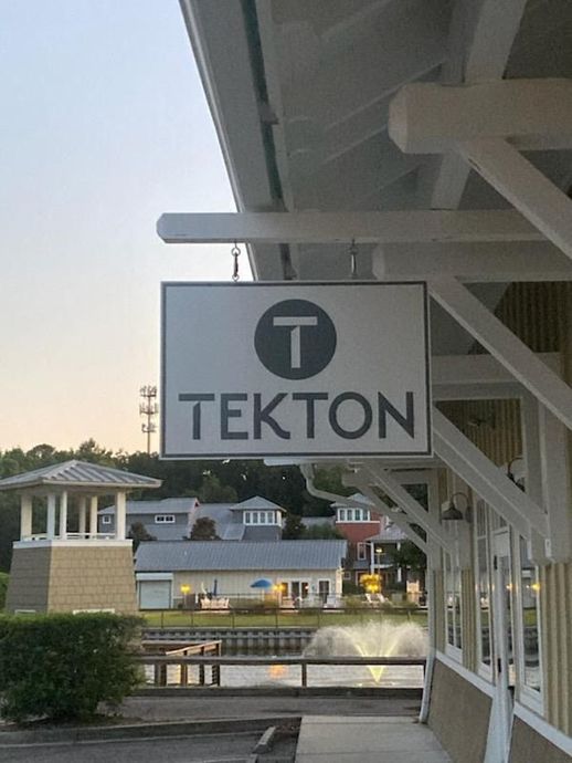 TEKTON sign hanging from a building canopy by a waterfront at dusk