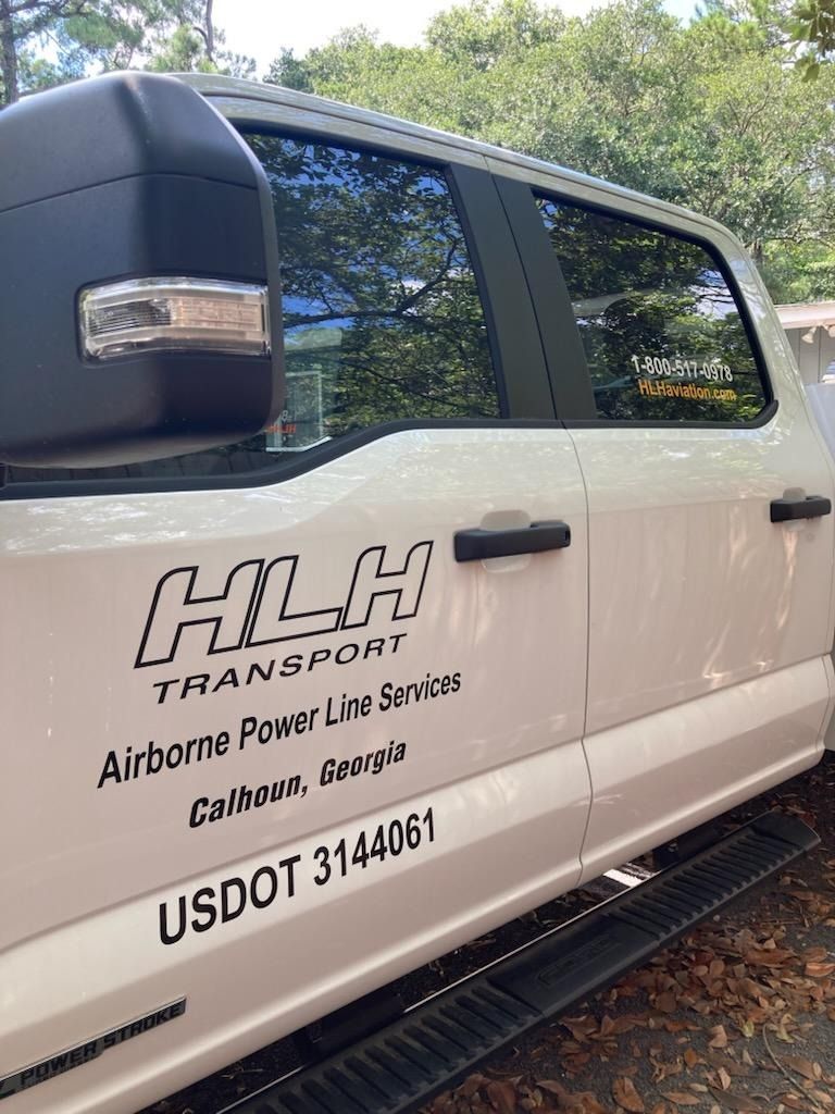 White HLH Transport truck with company text on the door, parked outdoors on a sunny day.
