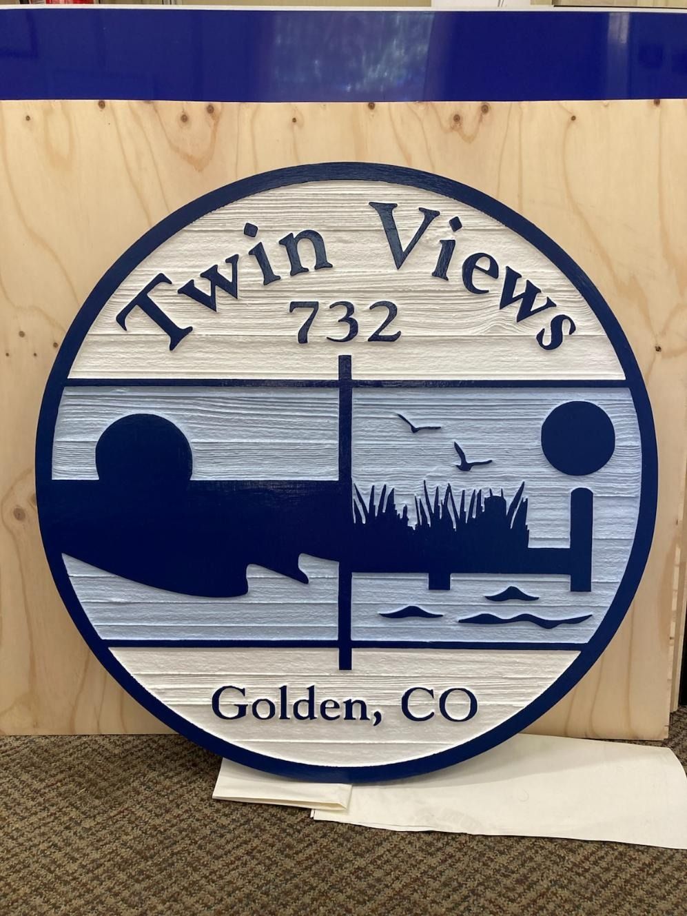 Round blue-and-white “Twin Views” sign with 732 and “Golden, CO” on a wood-paneled wall.