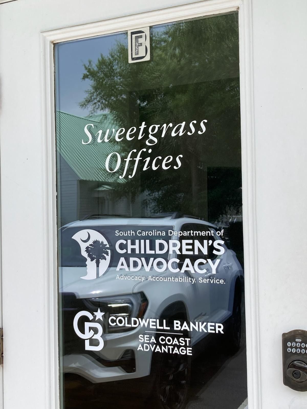 Glass office door with “Sweetgrass Offices” and tenant signs for Children’s Advocacy and Coldwell Banker.
