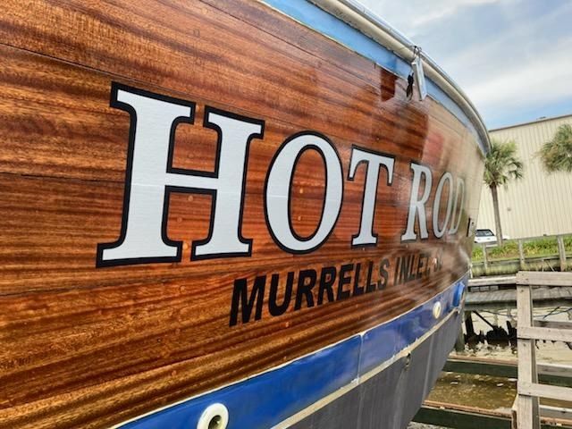 Wood-grain boat hull with “HOTROD MURRELL’S” lettering near a dock or yard