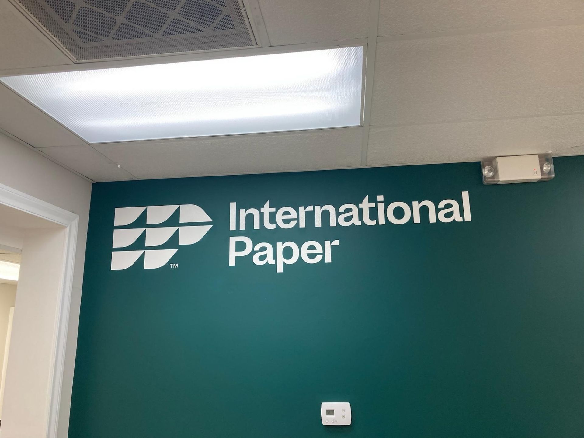 International Paper logo on a teal office wall under fluorescent ceiling lights