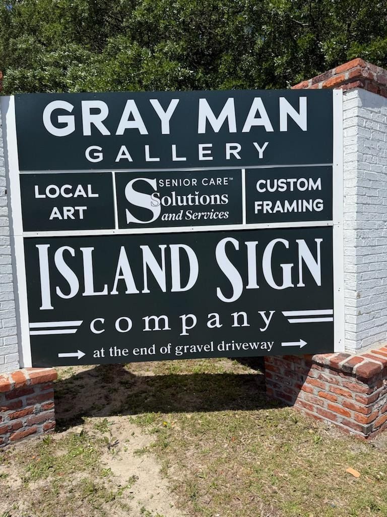 Sign for Gray Man Gallery and Island Sign Company on a brick post, with local art and framing text.