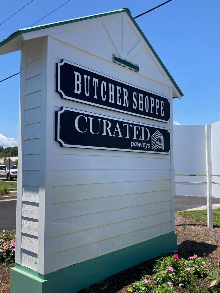 Small white roadside building with green trim and signs reading “Butcher Shoppe” and “Crated”