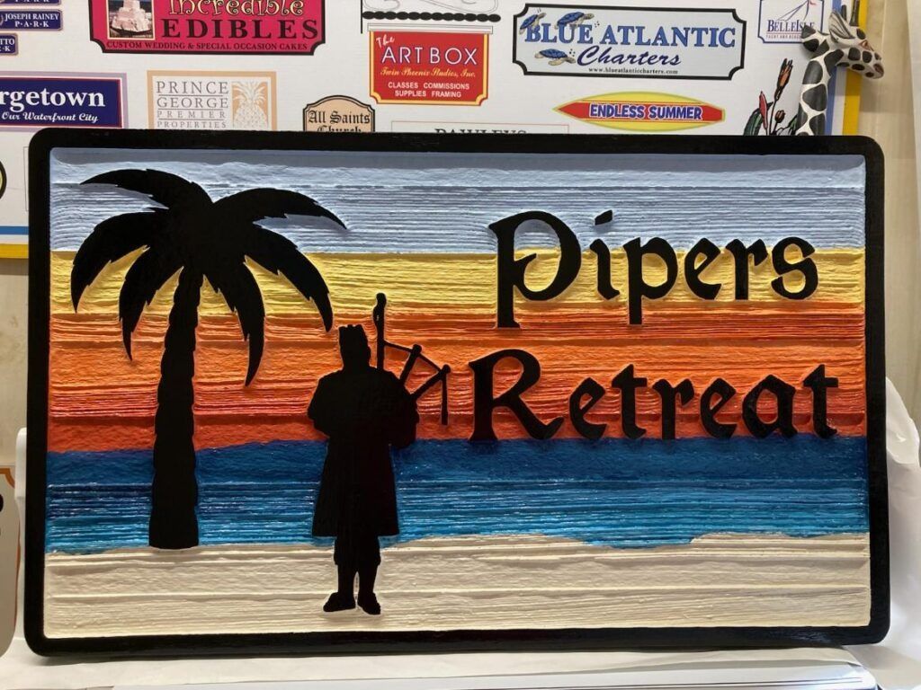 Sign reading “Pipers Retreat” with a sunset beach scene, palm tree, and silhouetted musician.