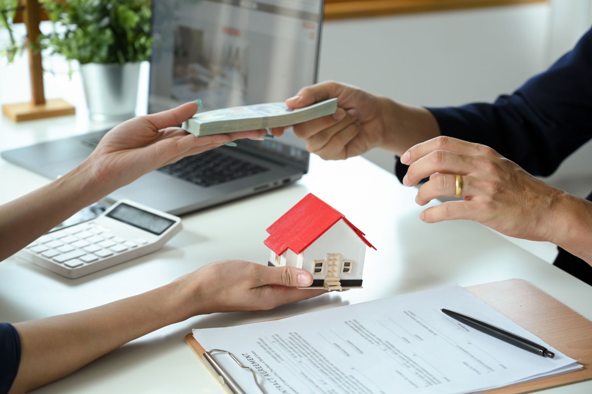 A woman is handing a money to another woman while holding a model house.