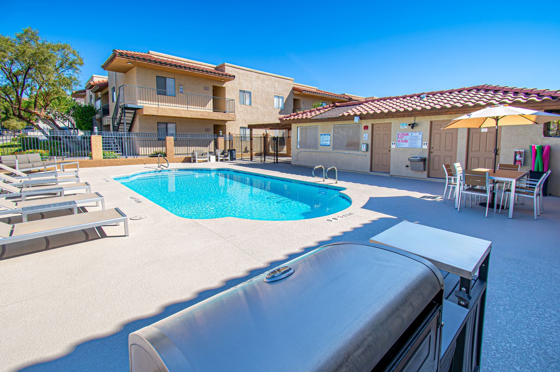 Backyard pool patio with lounge chairs and a house under a bright blue sky