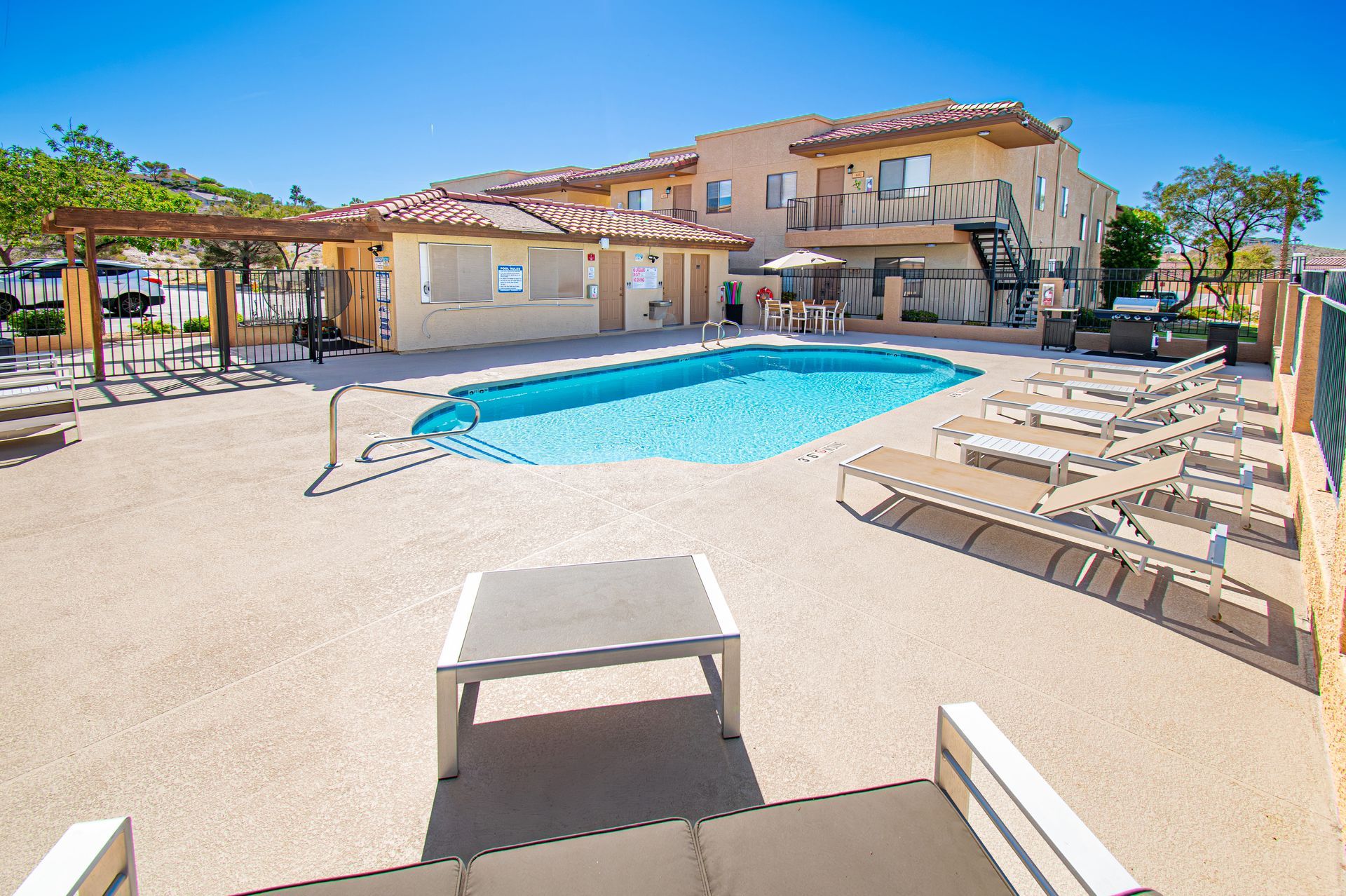 Sunlit villa patio with a blue pool, lounge chairs, and terracotta-roofed house in the background