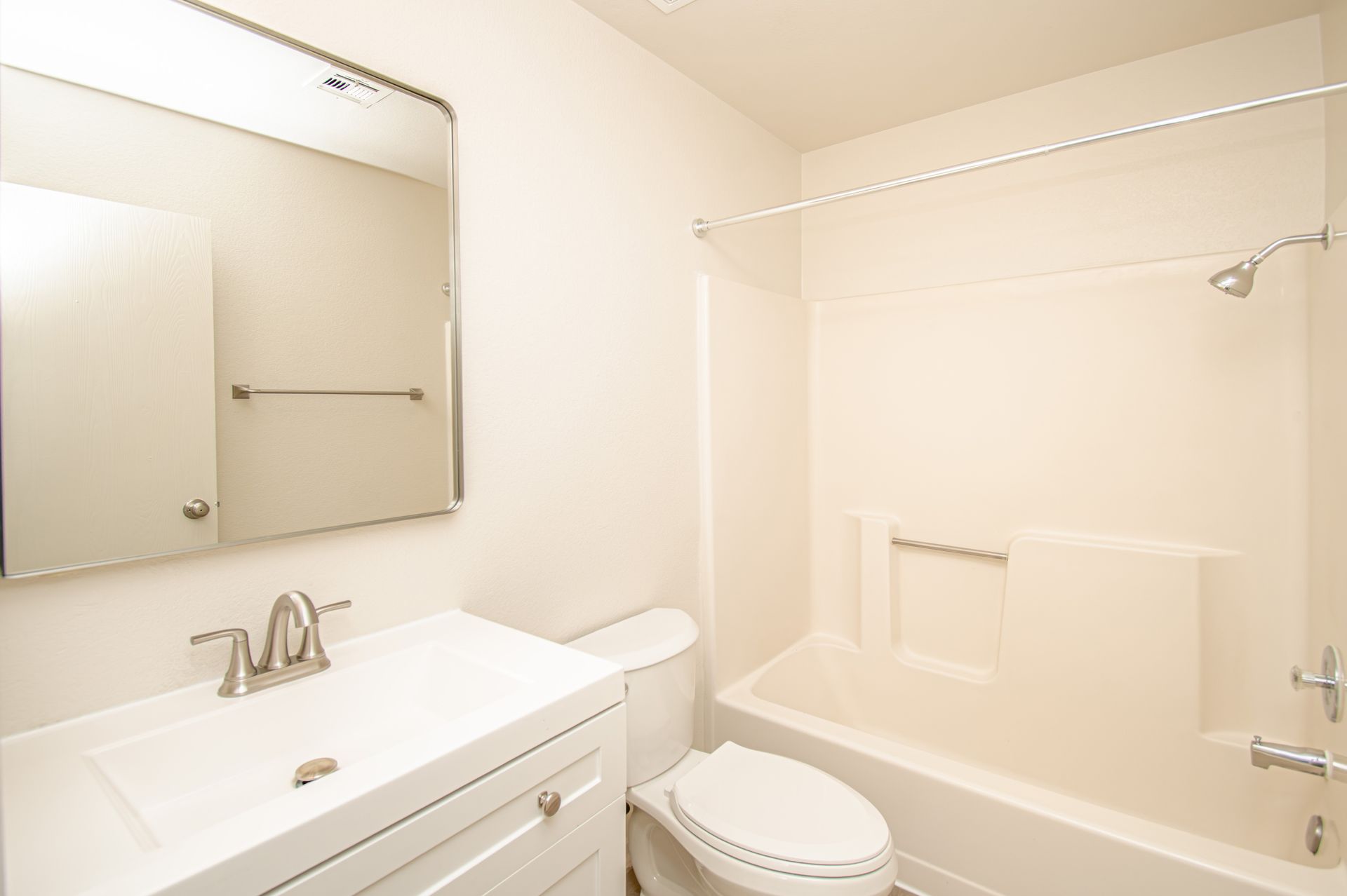 Bright bathroom with white vanity, mirror, toilet, and bathtub/shower area.