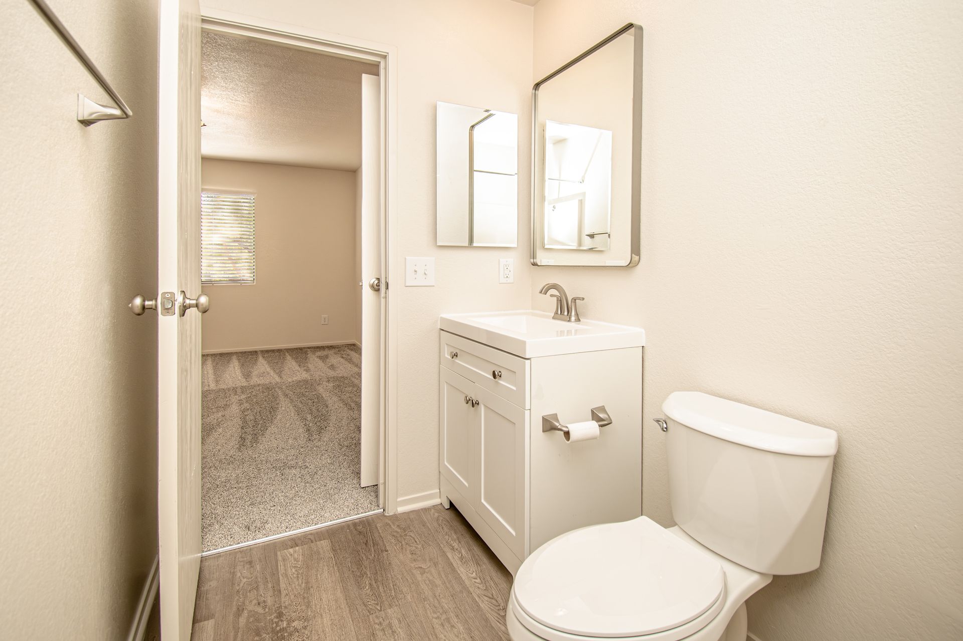 Small bathroom with toilet, vanity sink, mirror, and open door to carpeted room
