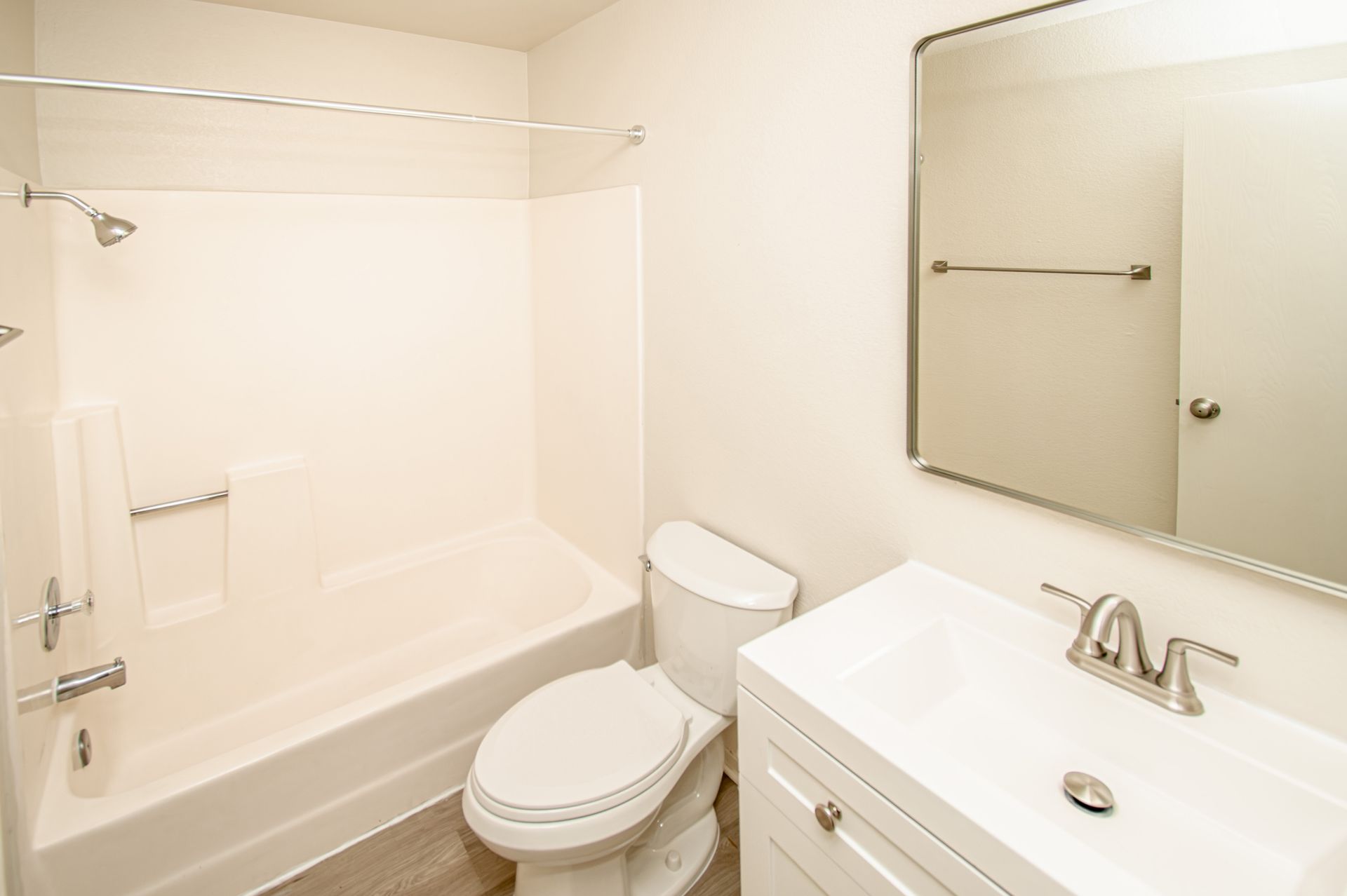 Bright white bathroom with bathtub, toilet, and vanity sink under a mirror
