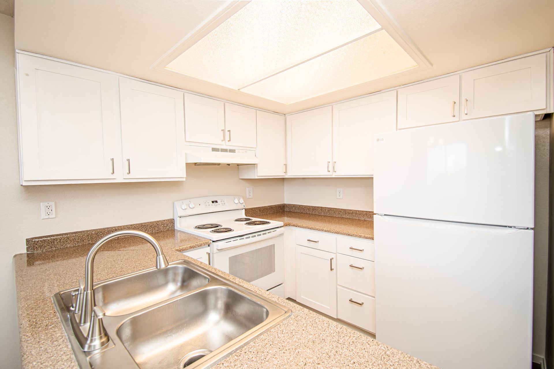 Bright white kitchen with granite counters, stainless sink, white cabinets, stove, and refrigerator