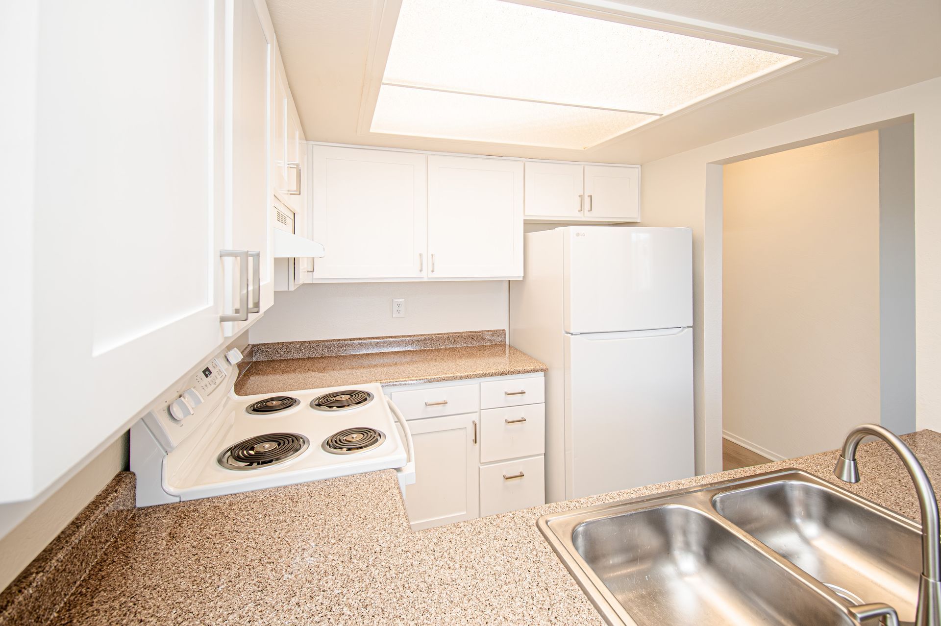 Bright white kitchen with speckled countertops, stove, refrigerator, and stainless-steel sink.
