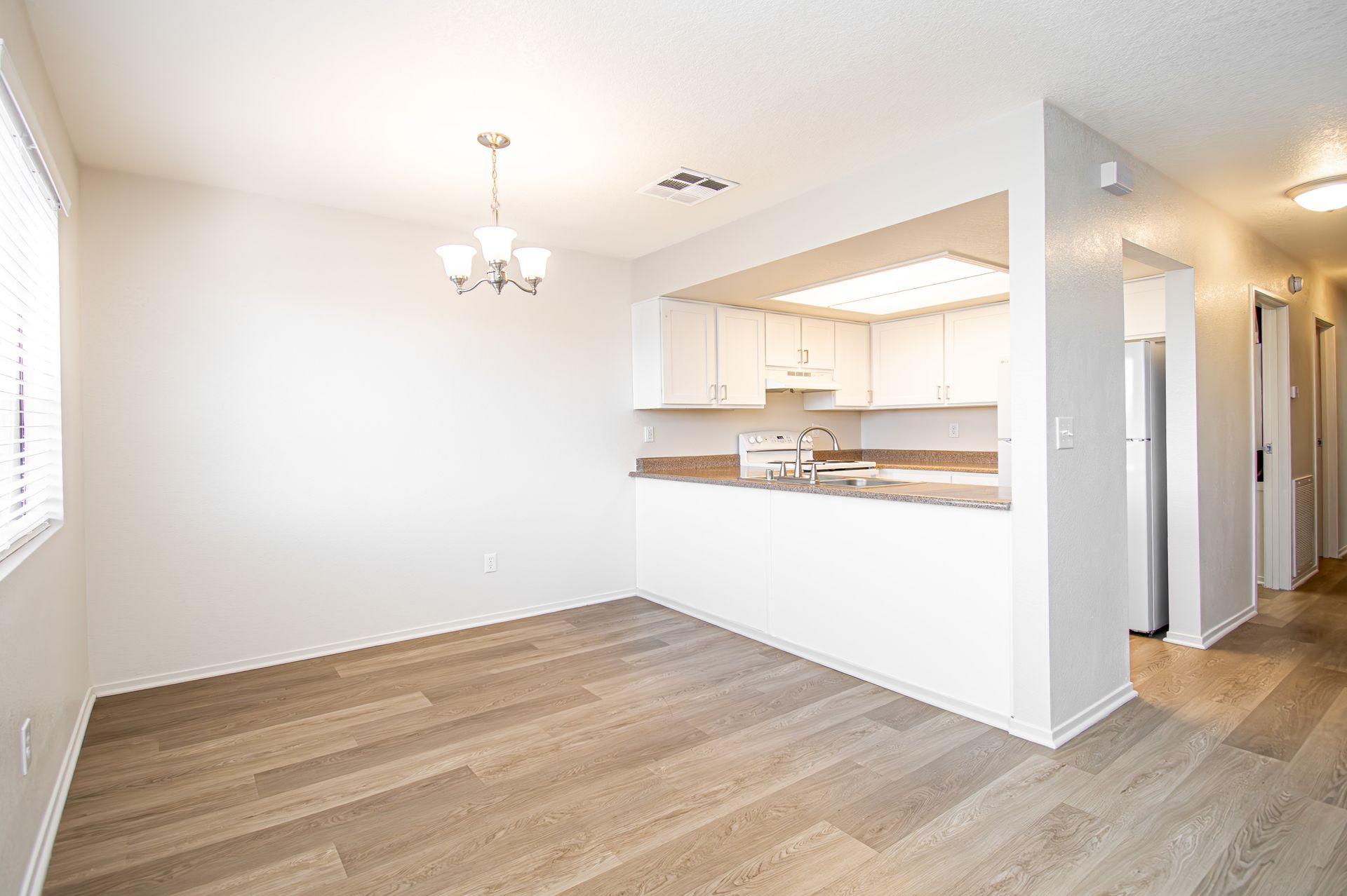 Bright empty dining area with wood floors, open kitchen pass-through, and hallway in a modern home.